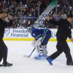 Workers carry a piece of broken glass off the ice past Vancouver Canucks goalie Ryan Miller during first period of an NHL hockey game in Vancouver, British Columbia, Monday, Dec. 22, 2014. (AP Photo/The Canadian Press, Darryl Dyck)