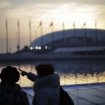 Visitors stand along the edge of the pool under the Olympic cauldron as the sun sets at the 2014 Winter Olympics, Friday, Feb. 21, 2014, in Sochi, Russia. (AP Photo/David Goldman)