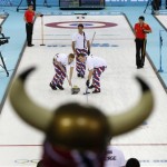 Norwegian curling fan Rune Eikeland, wearing viking horns, watches his countrymen Haavard Vad Petersson, left, and Christoffer Svae sweep in front of a rock delivered by skip Thomas Ulsrud during men's curling competition against China at the 2014 Winter Olympics, Friday, Feb. 14, 2014, in Sochi, Russia. (AP Photo/Robert F. Bukaty)