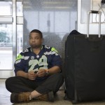 David Thomas, of Arlington, Tex., and a Seattle Seahawks fan, waits on the floor of Terminal B at LaGuardia airport , Monday, Feb. 3, 2014, in New York. Several inches of snow in the eastern United States on Monday disrupted air traffic. (AP Photo/John Minchillo)