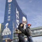 Pedestrians cross the street in front of a Super Bowl XLVI logo displayed on the side of a downtown Indianapolis hotel, Friday, Feb. 3, 2012. The New England Patriots are scheduled to play the New York Giants in Super Bowl XLVI on Feb. 5. (AP Photo/David Duprey)