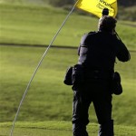 PGA tour photographer Stan Badz shoots the flag on the 11th green as it tilts in the wind before the first round at the Tournament of Champions PGA golf tournament on Sunday, Jan. 6, 2013, in Kapalua, Hawaii. Play was to have started two days earlier but was delayed because of rain and high winds. (AP Photo/Elaine Thompson)
