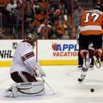 Philadelphia Flyers' Wayne Simmonds, right, jumps to let the puck go under him as Phoenix Coyotes' Thomas Greiss, left, defends the goal in the second period of an NHL hockey game on Friday, Oct. 11, 2013, in Philadelphia. (AP Photo/Tom Mihalek)