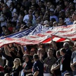 Fans hold the United States flag during the national anthem prior to the NASCAR Sprint Cup Series auto race, Sunday, Nov. 11, 2012, at Phoenix International Raceway in Avondale, Ariz. (AP Photo/Matt York)
