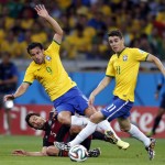 Brazil's Fred, left, falls over Germany's Mats Hummels as Brazil's Oscar, right, looks to the ball during the World Cup semifinal soccer match between Brazil and Germany at the Mineirao Stadium in Belo Horizonte, Brazil, Tuesday, July 8, 2014. (AP Photo/Frank Augstein)