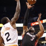 Miami Heat's Dwyane Wade (3) gets a shot off over Phoenix Suns' Eric Bledsoe (2) during the first half of an NBA basketball game Tuesday, Dec. 9, 2014, in Phoenix. (AP Photo/Ross D. Franklin)