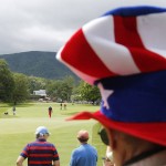 A fan with an Uncle Sam hat watches Tiger Woods, left, and Morgan Hoffmann, center, walk up to the first green during the third round of the Greenbrier Classic golf tournament at the Greenbrier Resort in White Sulphur Springs, W.Va., Saturday, July 4, 2015. Rain caused delays in play. (AP Photo/Steve Helber)
