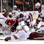 A puck that hit the shoulder of New Jersey Devils left wing Ryane Clowe, center, enters the net of Phoenix Coyotes goalie Thomas Greiss, left, of Germany, during the second period of an NHL hockey game, Thursday, March 27, 2014, in Newark, N.J. (AP Photo/Julio Cortez)
