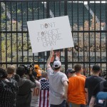 Brendan Hurson, of Baltimore, holds a sign as fans view a baseball game between the Baltimore Orioles and Chicago White Sox Wednesday, April 29, 2015, from outside of Oriole Park at Camden Yards in Baltimore. The game was played in an empty stadium amid unrest in Baltimore over the death of Freddie Gray while in police custody. (AP Photo/Matt Rourke)
