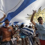 Uruguay soccer fans cheer under their nation's flag before the start of their team's World Cup game against Costa Rica inside the FIFA Fan Fest area on Copacabana beach in Rio de Janeiro, Brazil, Saturday, June 14, 2014. (AP Photo/Silvia Izquierdo)
