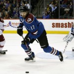 Colorado Avalanche defenseman Bard Stuart, center, pursues the puck to clear it from his team's zone as Arizona Coyotes left wing Lauri Korpikoski, left, of Finland, and Avlaanche goalie Semyon Varlamov, of Russia, look on in the first period of an NHL hockey game Monday, Feb. 16, 2015, in Denver. (AP Photo/David Zalubowski)