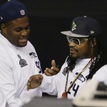 Seattle Seahawks' Marshawn Lynch, right, talks to teammate Brandon Mebane as he makes his way out off the floor at the beginning of media day for NFL Super Bowl XLIX football game Tuesday, Jan. 27, 2015, in Phoenix. (AP Photo/Charlie Riedel)
