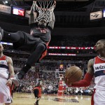Toronto Raptors forward Amir Johnson (15) hangs drom the rim after a dunk, between Washington Wizards center Marcin Gortat (4) guard Bradley Beal (3) during the second half of Game 3 in an NBA basketball first-round playoff series, Friday, April 24, 2015, in Washington. The Wizards won 106-99. (AP Photo/Alex Brandon)