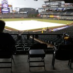 A lone fan sits silhouetted against the diamond covered by a tarpulin as light rain delays the start of the first inning of a baseball game between the Arizona Diamondbacks and Colorado Rockies Monday, May 4, 2015, in Denver. (AP Photo/David Zalubowski)