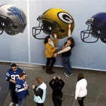 Football fans pose in front of the mural of NFL football helmets at the Super Bowl Village in Indianapolis, Friday, Feb. 3, 2012. The New England Patriots will face the New York Giants on Sunday, Feb. 5, in Super Bowl XLVI . (AP Photo/Michael Conroy)